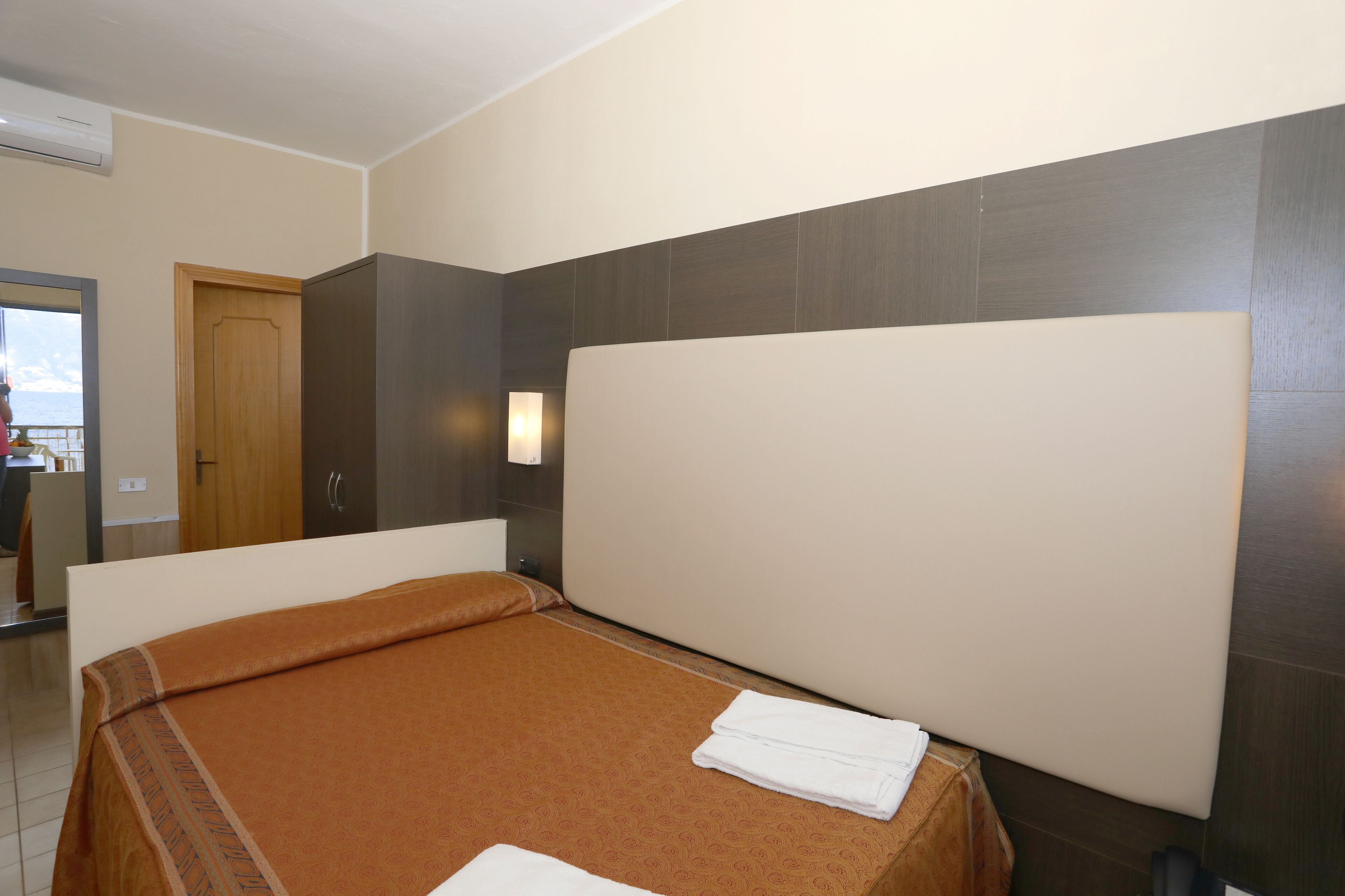 Une chambre d’hôtel avec un lit, une porte en bois, une armoire et une salle de bain visible au fond.