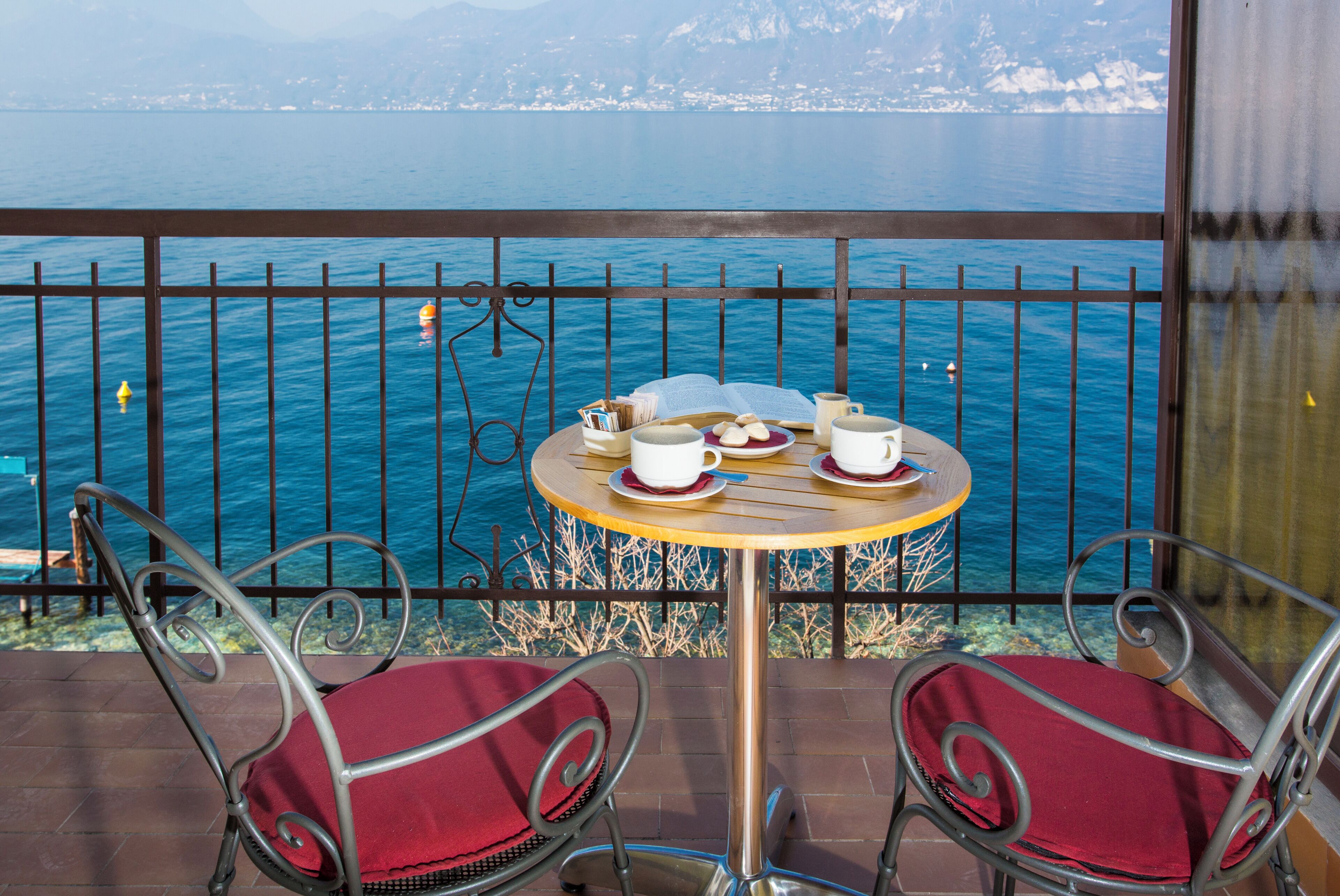 A balcony with a table set for two, overlooking a body of water and distant mountains.