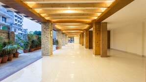 Un pasillo con vigas y columnas de madera, plantas en macetas y vistas de edificios residenciales.
