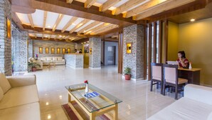 Un vestíbulo amplio con techo alto, paredes de piedra y vigas de madera. Hay zonas de estar con sofás y un mostrador de recepción.