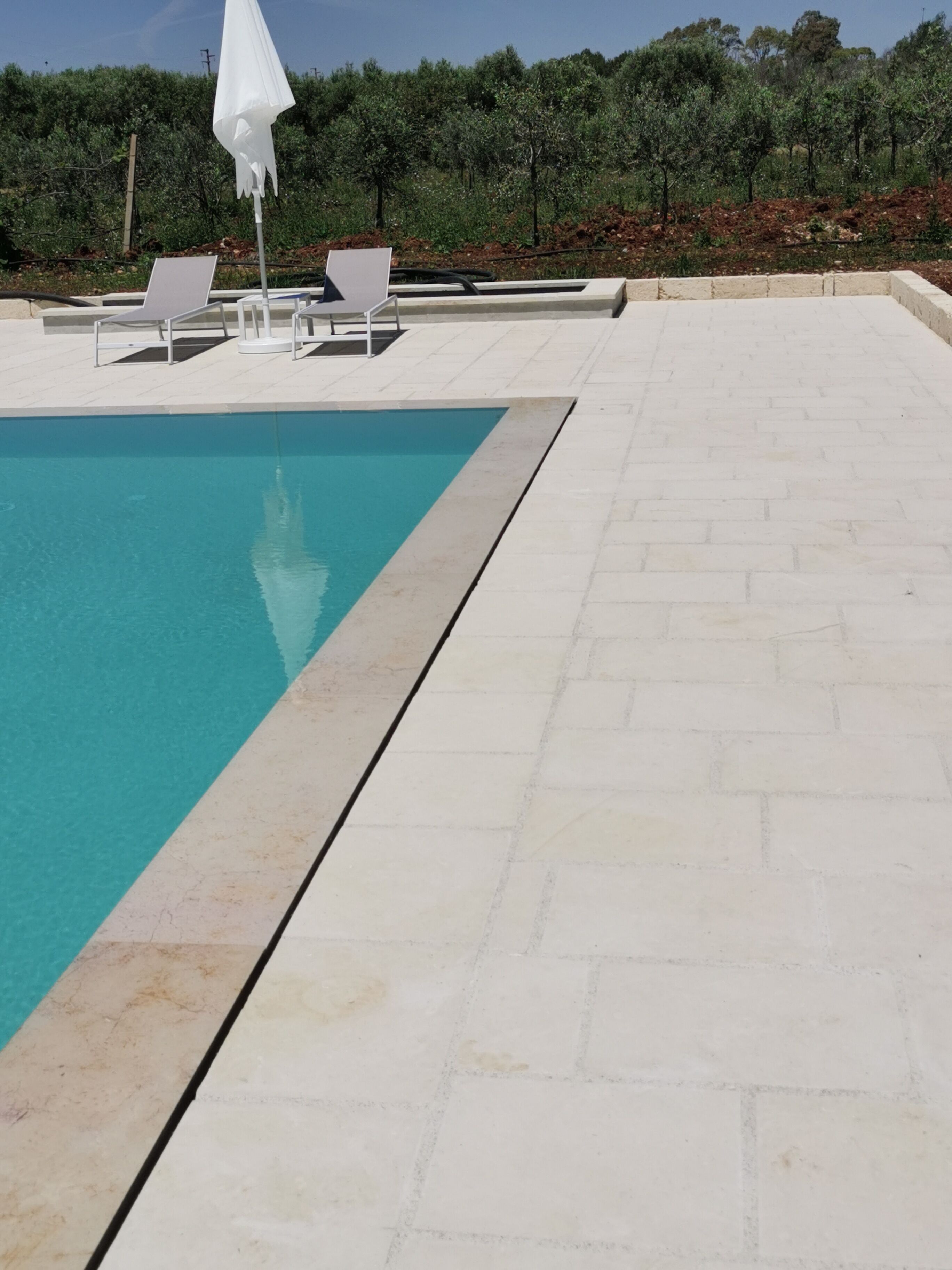 A swimming pool with two lounge chairs and a white umbrella.