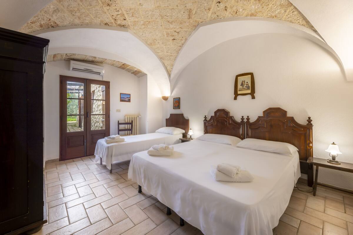 Une chambre d’hôtel avec deux lits, une armoire en bois, une porte donnant sur l’extérieur et un plafond en pierre.