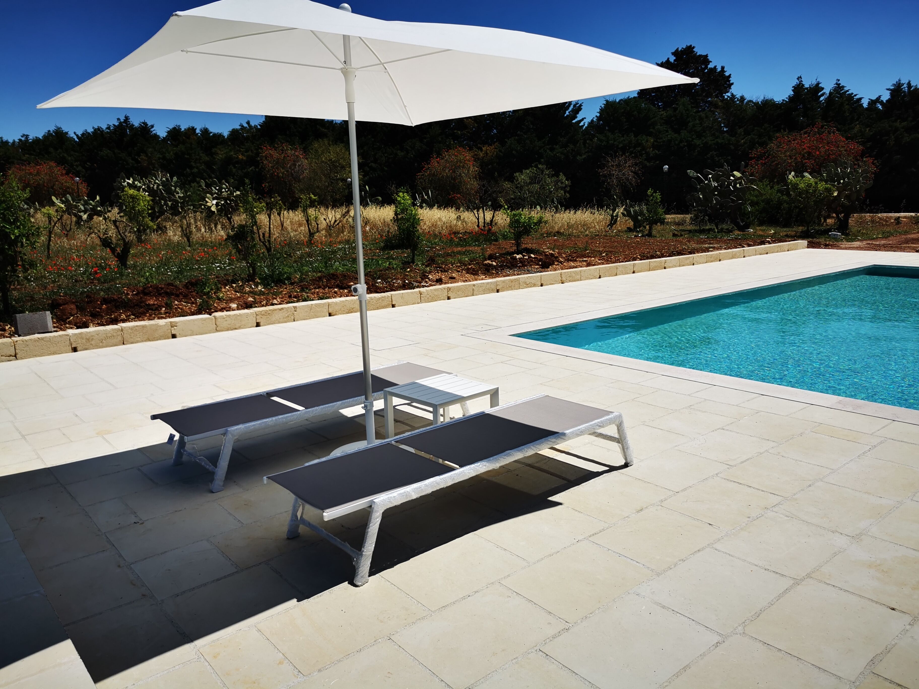 Un área junto a la piscina con dos sillas de descanso y una sombrilla blanca.