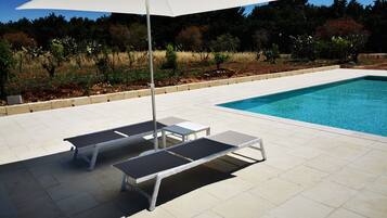 Un área junto a la piscina con dos sillas de descanso y una sombrilla blanca.