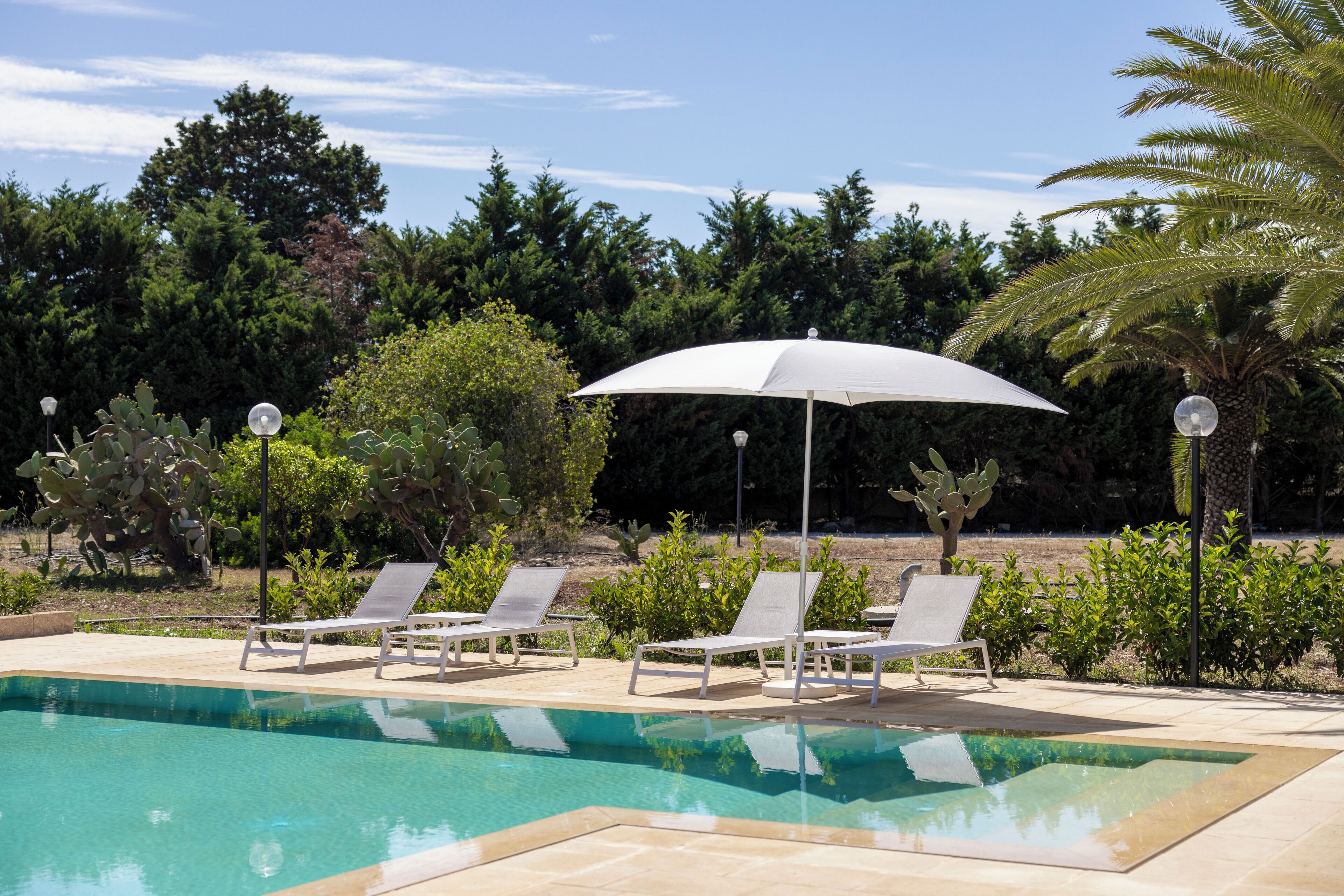 Un'area piscina con quattro sdraio e un ombrellone grande.