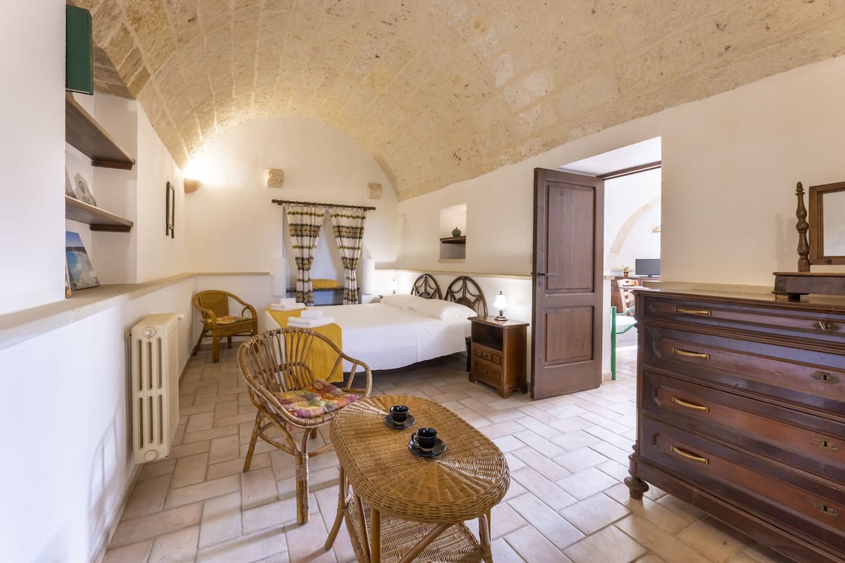 Une chambre confortable avec un lit, des meubles en osier, une commode et un radiateur.