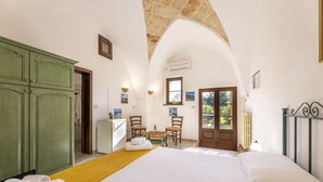 Hotelkamer met een groot bed, een groene garderobe, een eettafel met stoelen en uitzicht door een gebogen doorgang.
