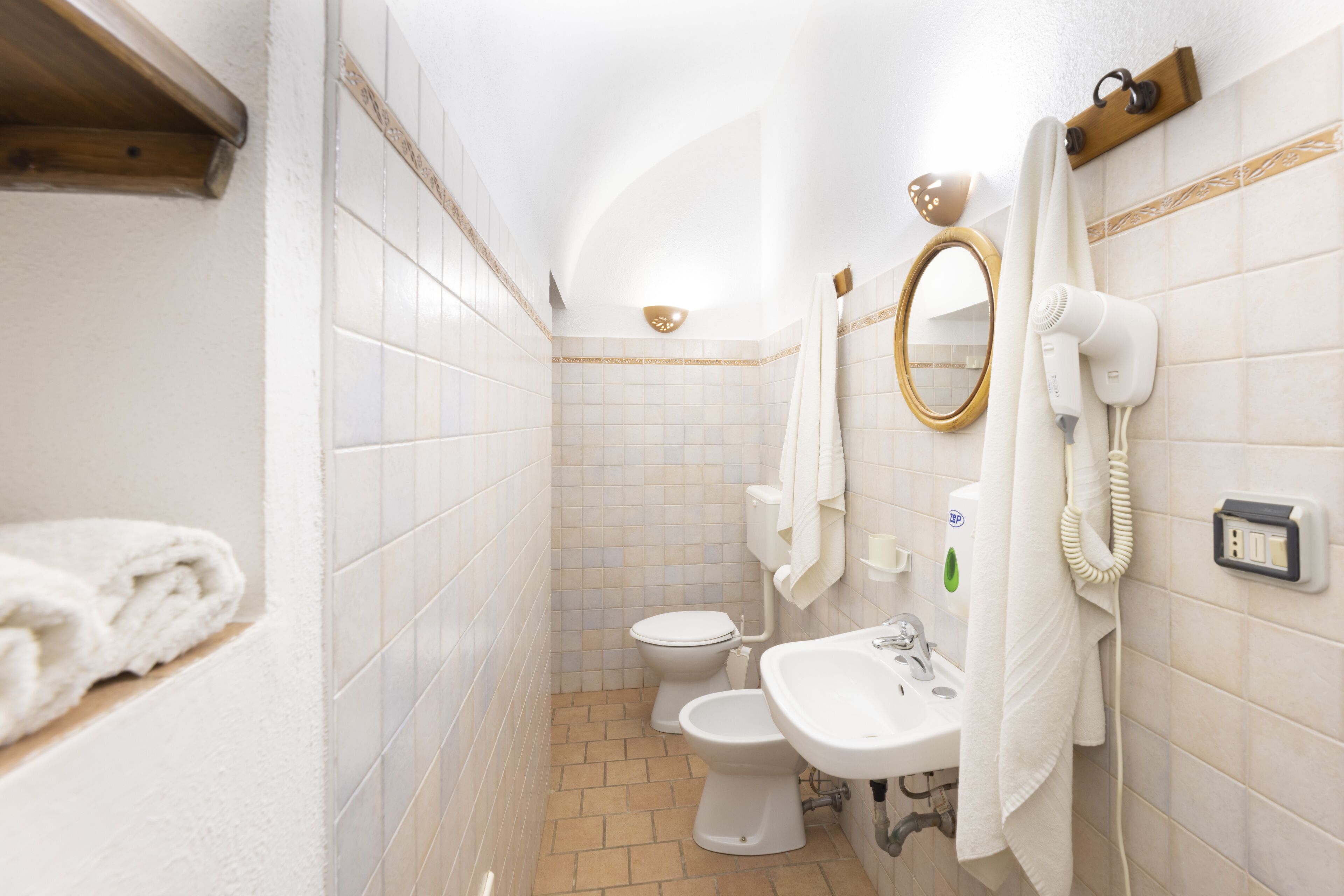 Baño con inodoro, bidé, lavamanos y un secador de pelo en la pared.