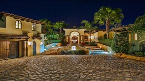 A courtyard with cobblestone flooring, a central fountain, and a building with arched windows and a tiled roof. - Casa Mar by Cabo Platinum (Cabo San Lucas)