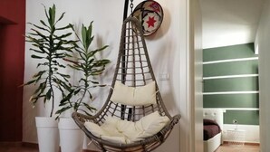 A hanging chair with a cushion, a potted plant, and a bed in a room with a green wall and a tiled floor. - B&B Casa Saba (Orosei)