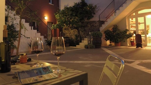 An outdoor seating area with tables, chairs, and wine glasses, surrounded by potted plants and a staircase leading to an upper level. - B&B Casa Saba (Orosei)