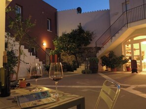 An outdoor seating area with tables, chairs, and wine glasses, surrounded by potted plants and a staircase leading to an upper level. - B&B Casa Saba (Orosei)
