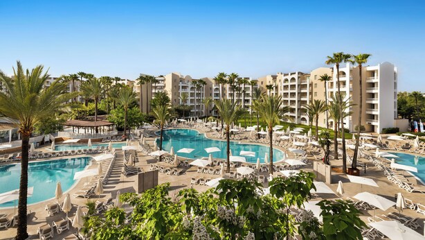 Un resort con varias piscinas, palmeras y tumbonas.