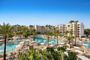 Resort com várias piscinas, palmeiras e espreguiçadeiras.