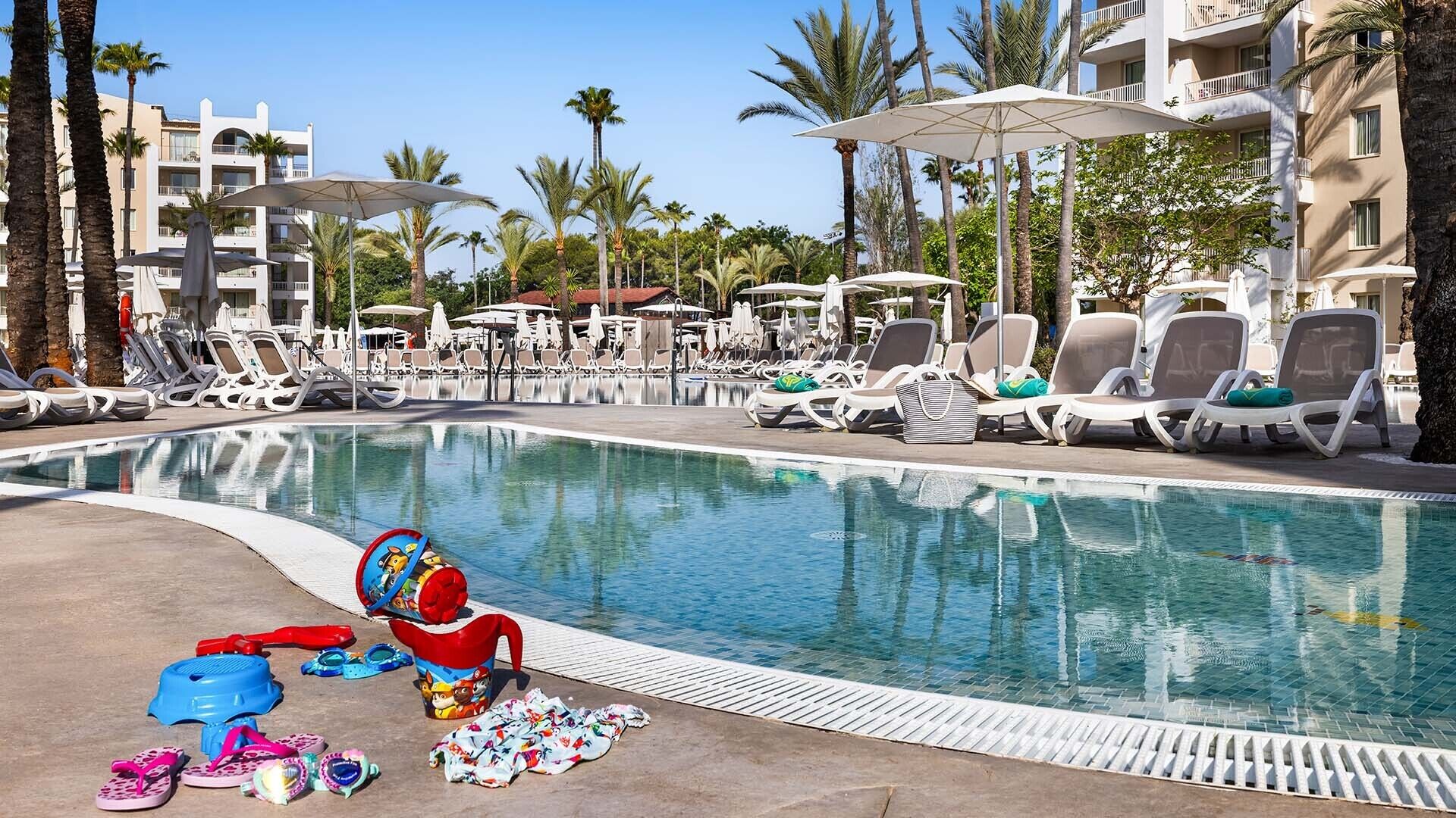 Ein Poolbereich mit Liegestühlen, Sonnenschirmen und einem klaren, blauen Pool.