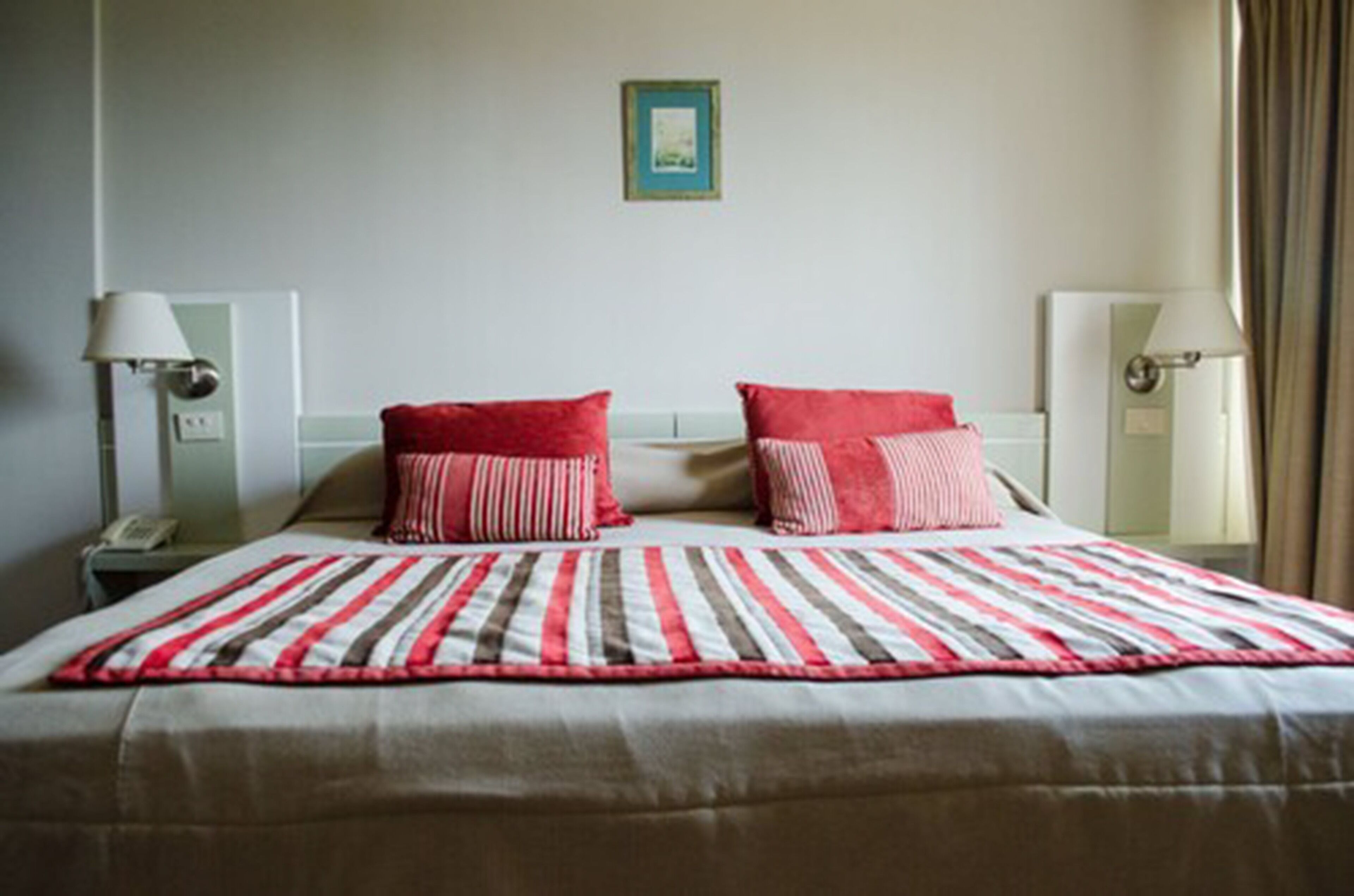 A hotel room with a bed, two bedside lamps, a nightstand, and a framed picture on the wall.