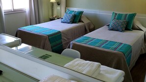 Ein Hotelzimmer mit zwei Betten, jeweils mit einem gestreiften Bettbezug und gemusterten Kissen, einem Nachttisch mit Lampe und einem Spiegel, der den Raum reflektiert.