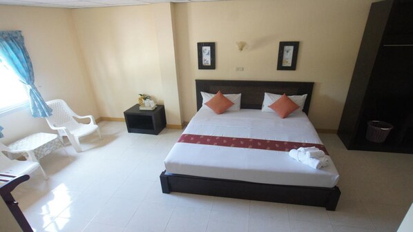 A hotel room with a bed, a small side table, a chair, and a window with curtains.