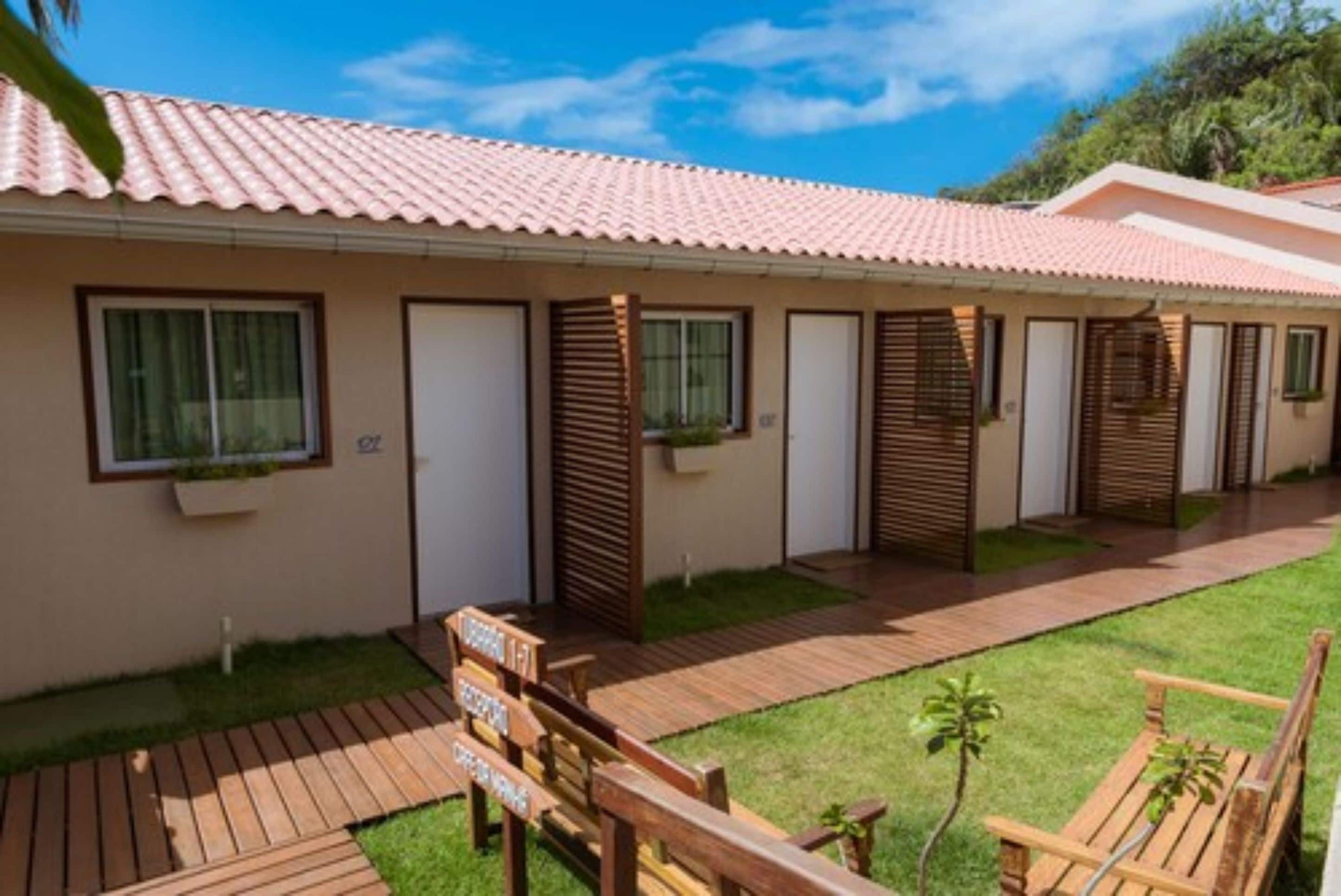 A row of single-story cabins with a tiled roof, each with a window and a door.