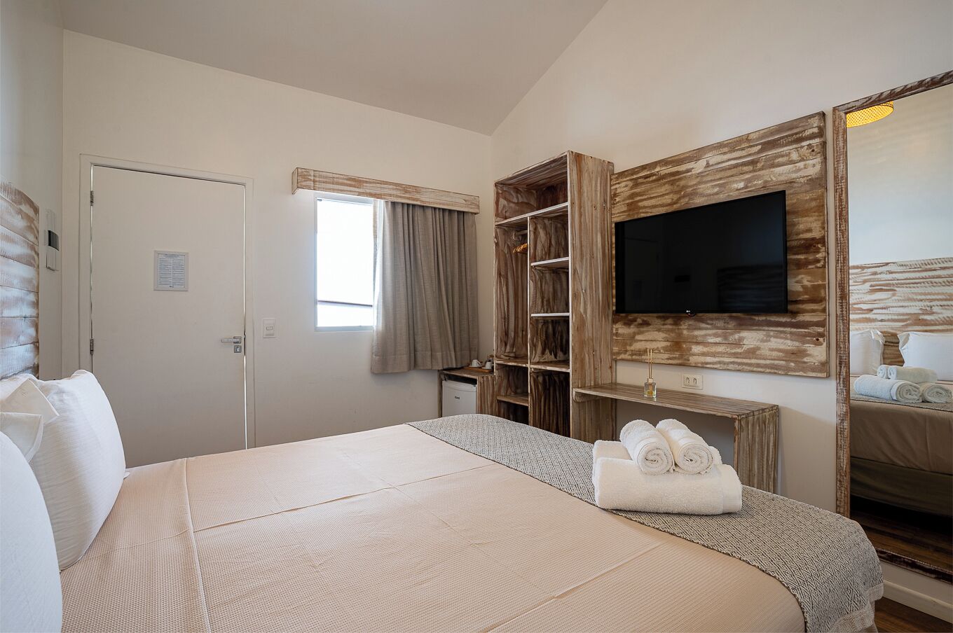 Quarto de hotel com cama grande, aparador de madeira, guarda-roupa e janela com cortinas.