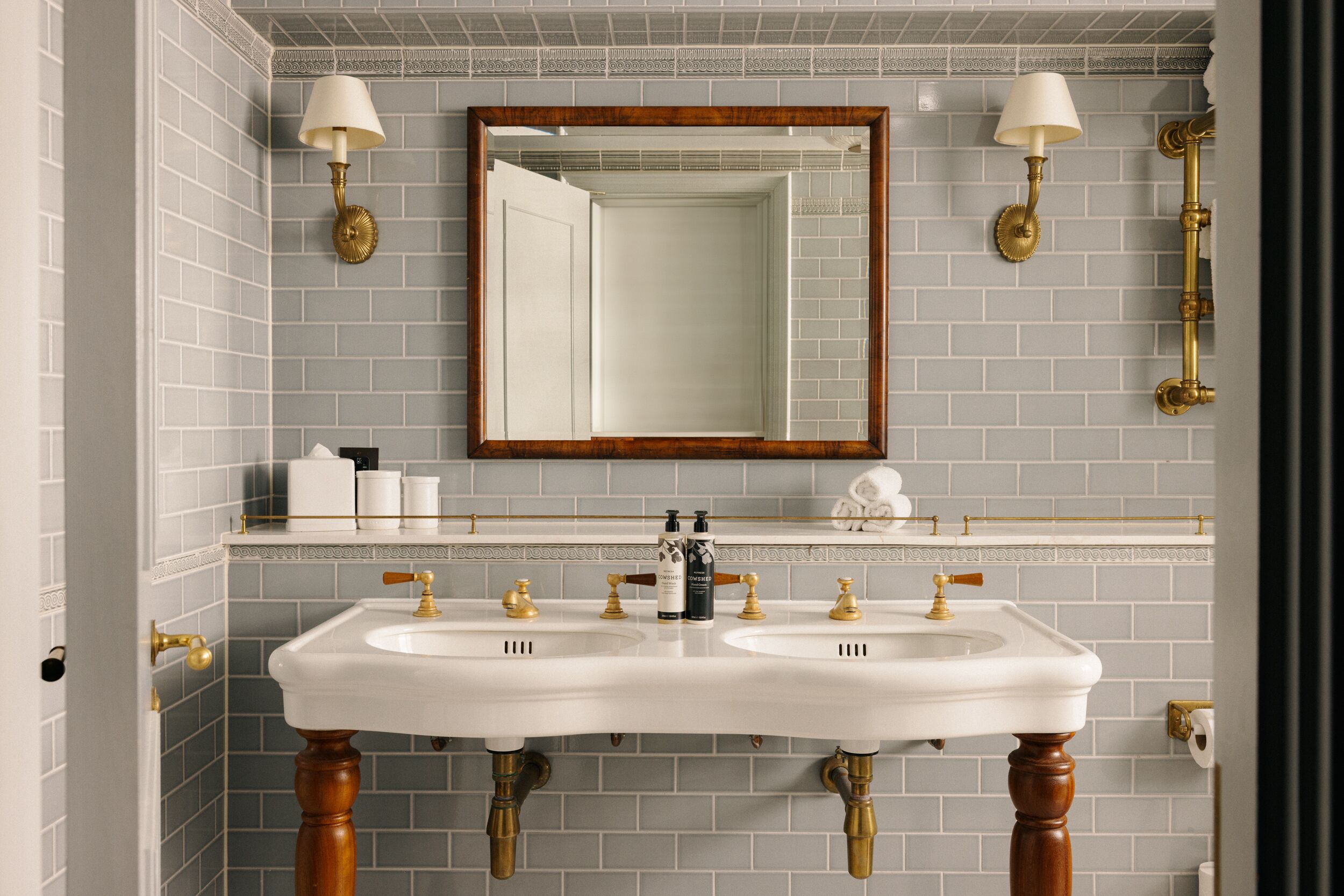 A bathroom with two sinks, a mirror, and wall-mounted lamps.