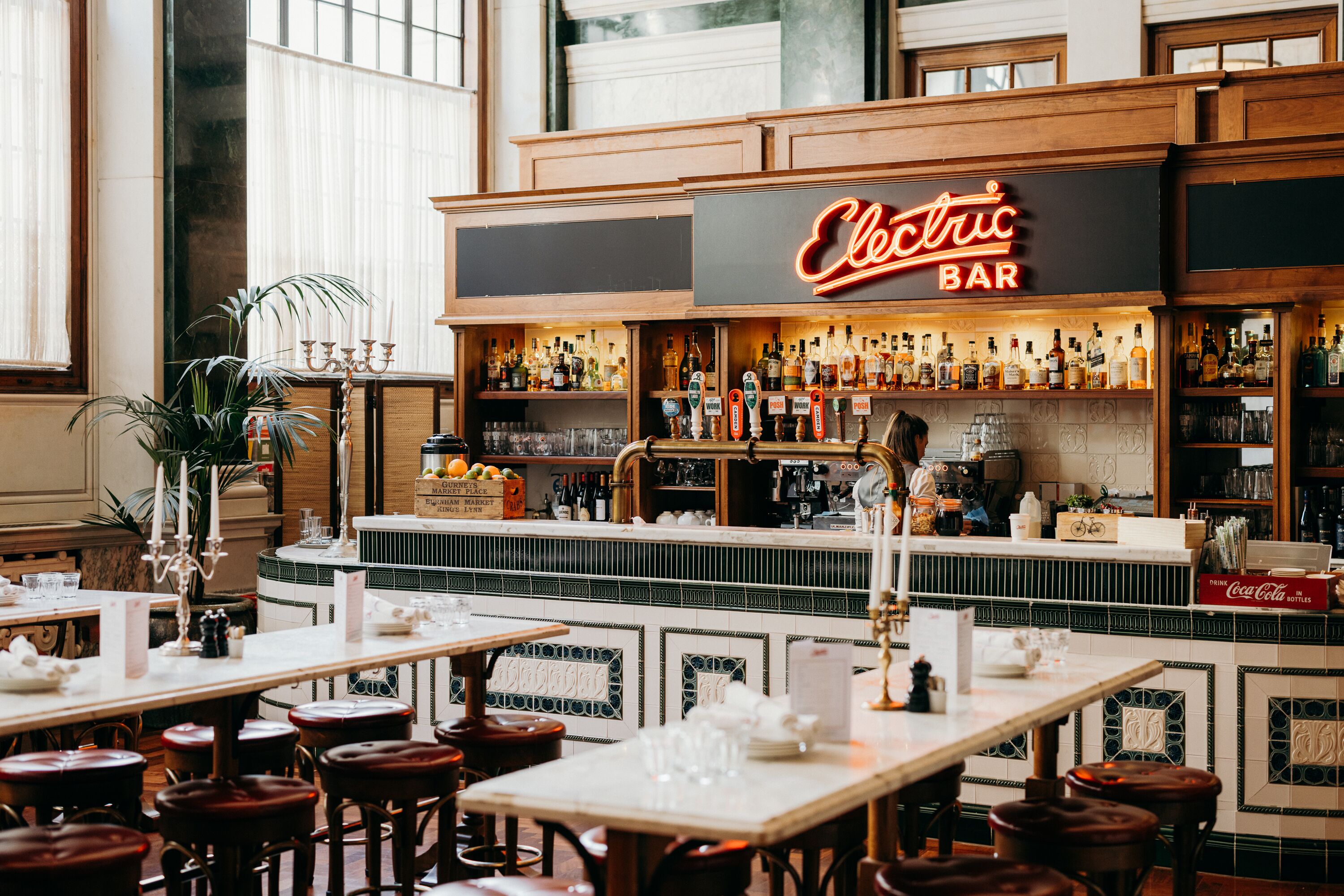 A bar area with a neon sign reading "Electric Bar," bar stools, and a variety of bottles on shelves.