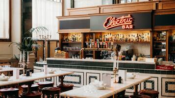 Uma área de bar com um letreiro de neon que diz 'Electric Bar', banquetas e diversos tipos de garrafas em prateleiras.