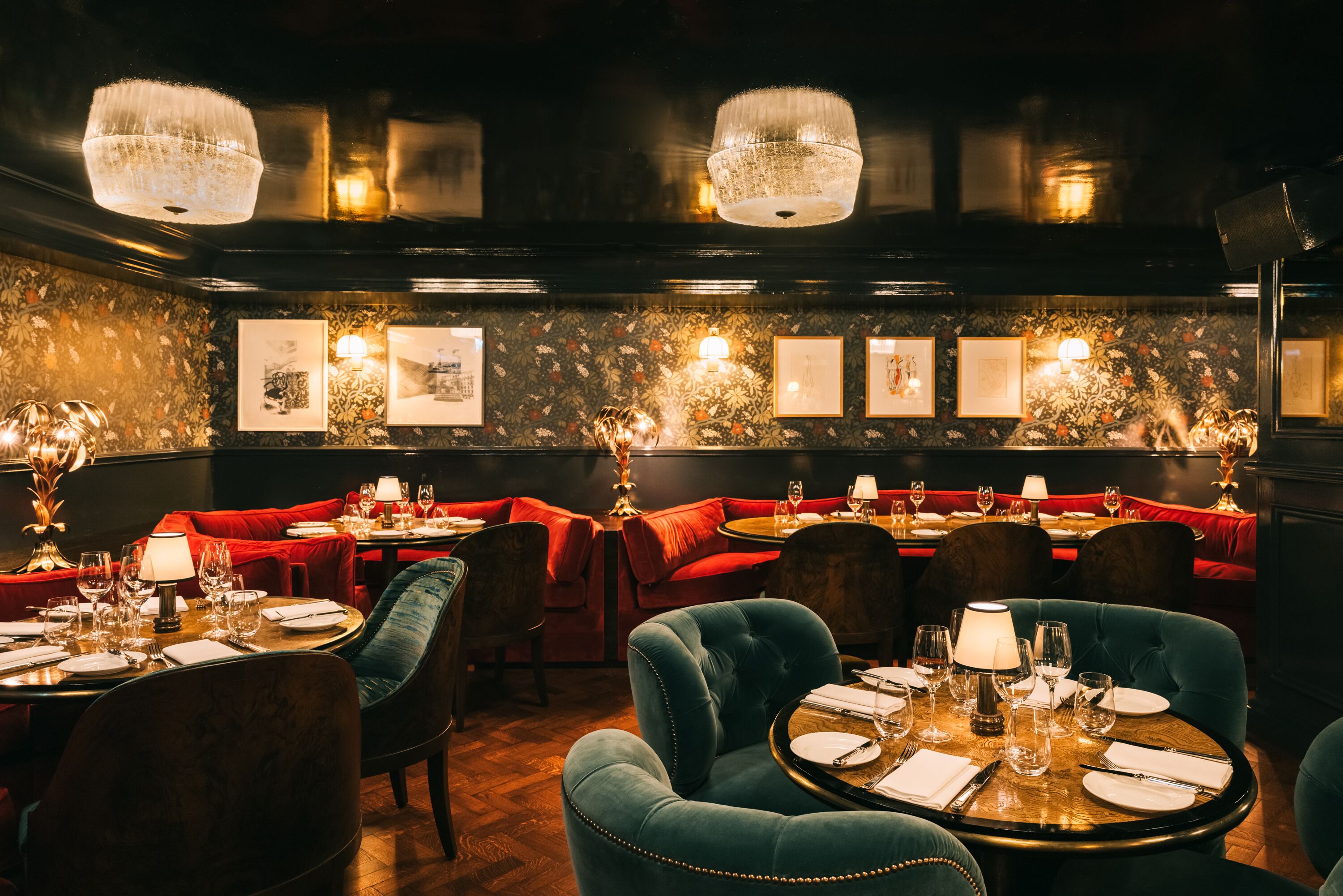Ein Restaurant in gedämpftem Licht mit rot gepolsterten Sitzecken, runden Tischen und Kristalllüstern.