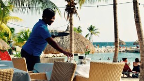 A beachside restaurant with wicker chairs and a thatched-roof umbrella. - Bohemi Villas (Sint Michiel)
