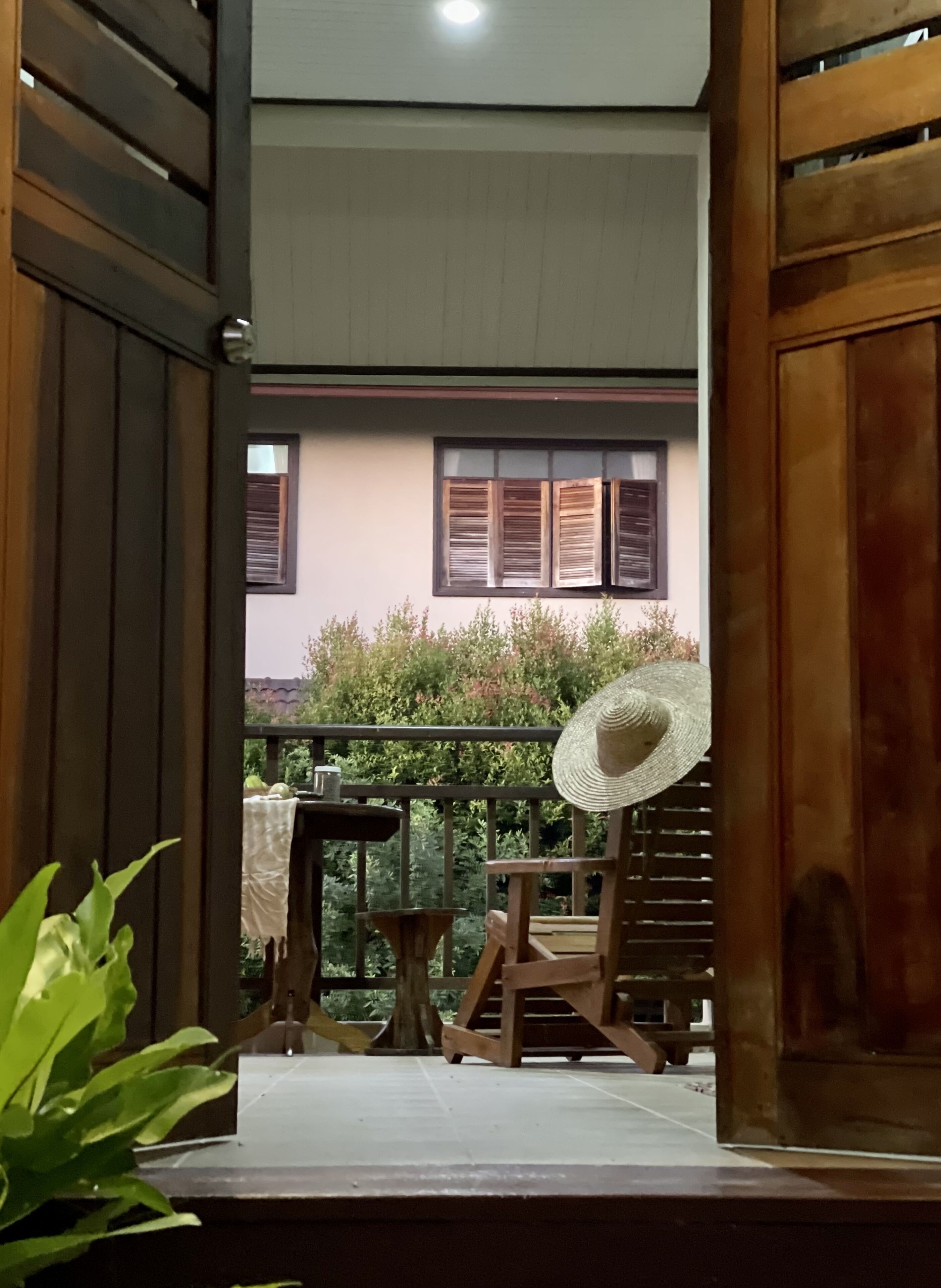 A wooden balcony with a table and a chair, a fan, and a view of a building with windows.