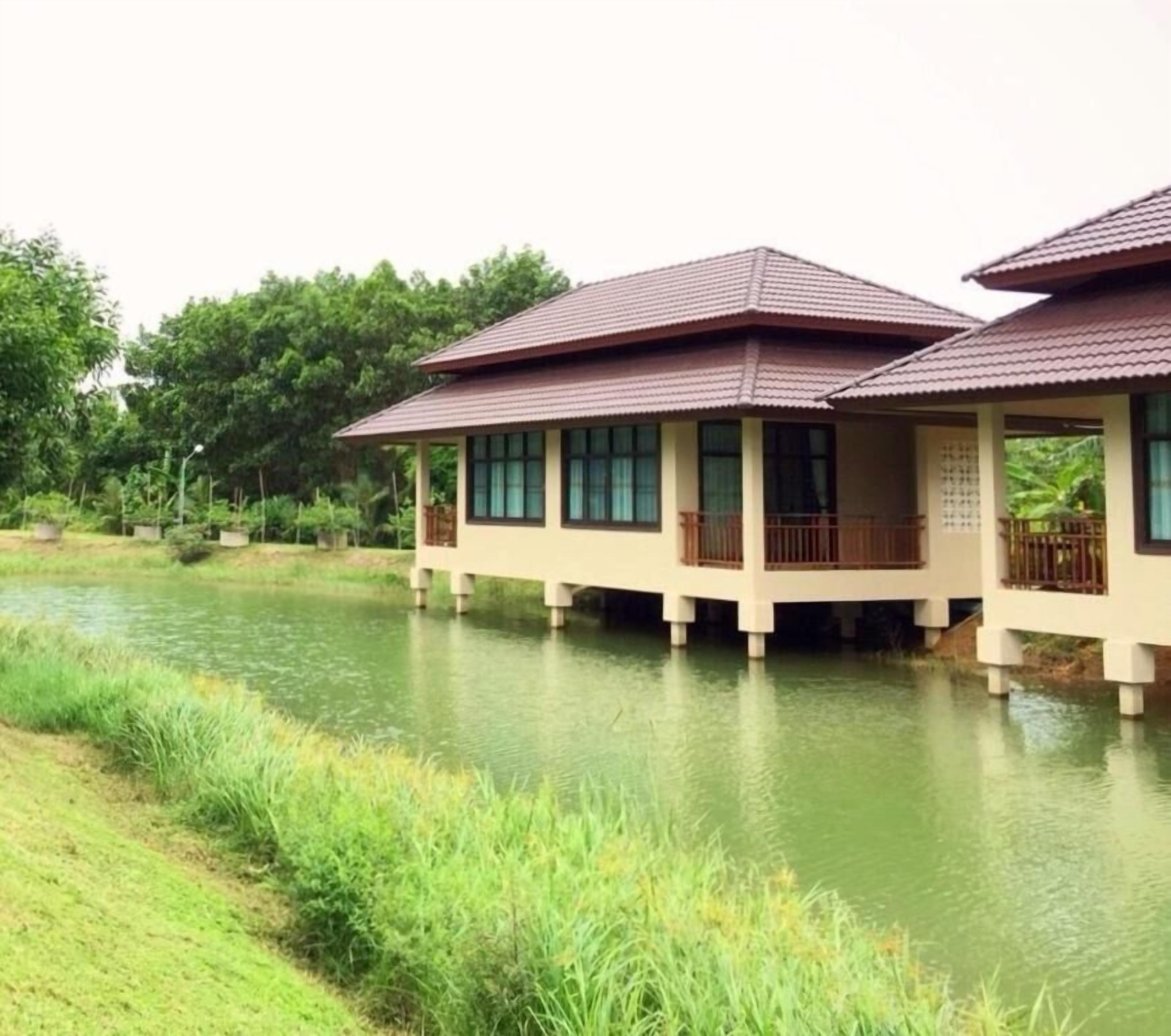 A row of two-story buildings with balconies, situated by a calm water body, likely a river or lake.