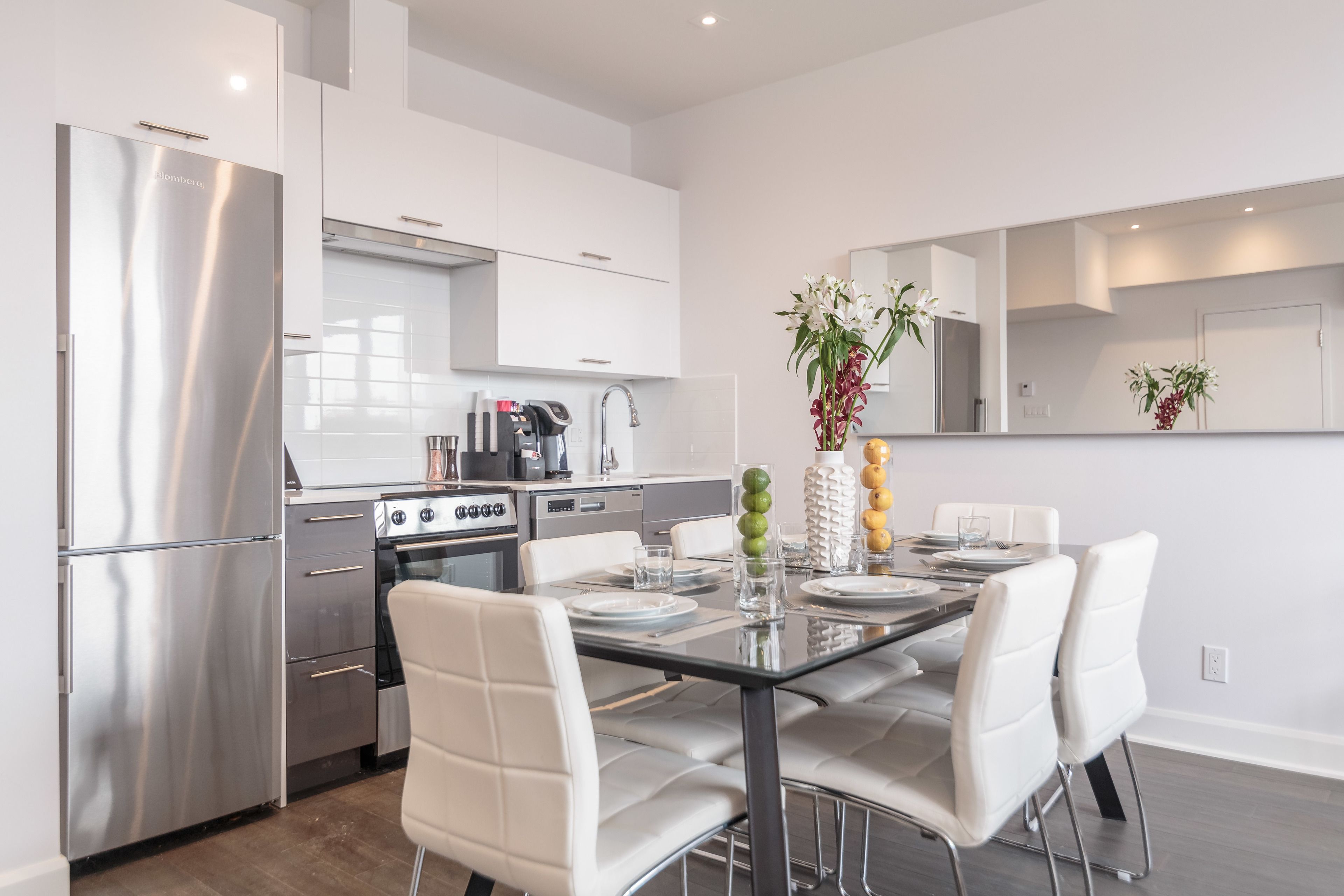 Een moderne keuken met roestvrijstalen apparatuur, een eettafel met witte stoelen en een vaas met bloemen.