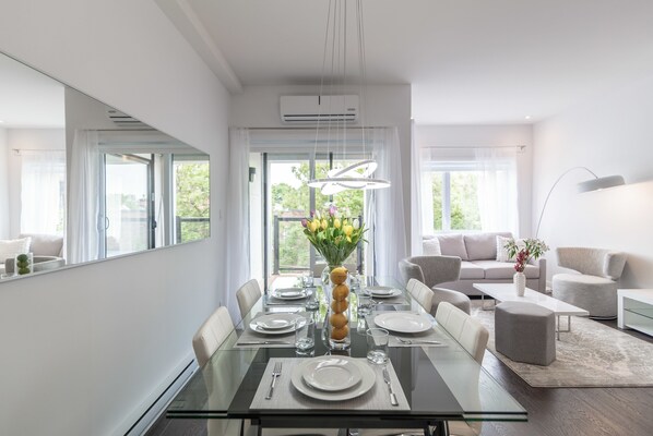 A modern dining room with a glass table, white plates, and a vase of flowers. - Parc Avenue Residence Mile End (Montreal)