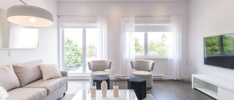 Una sala de estar moderna con un sofá, dos sillones, una mesa de centro y un televisor.