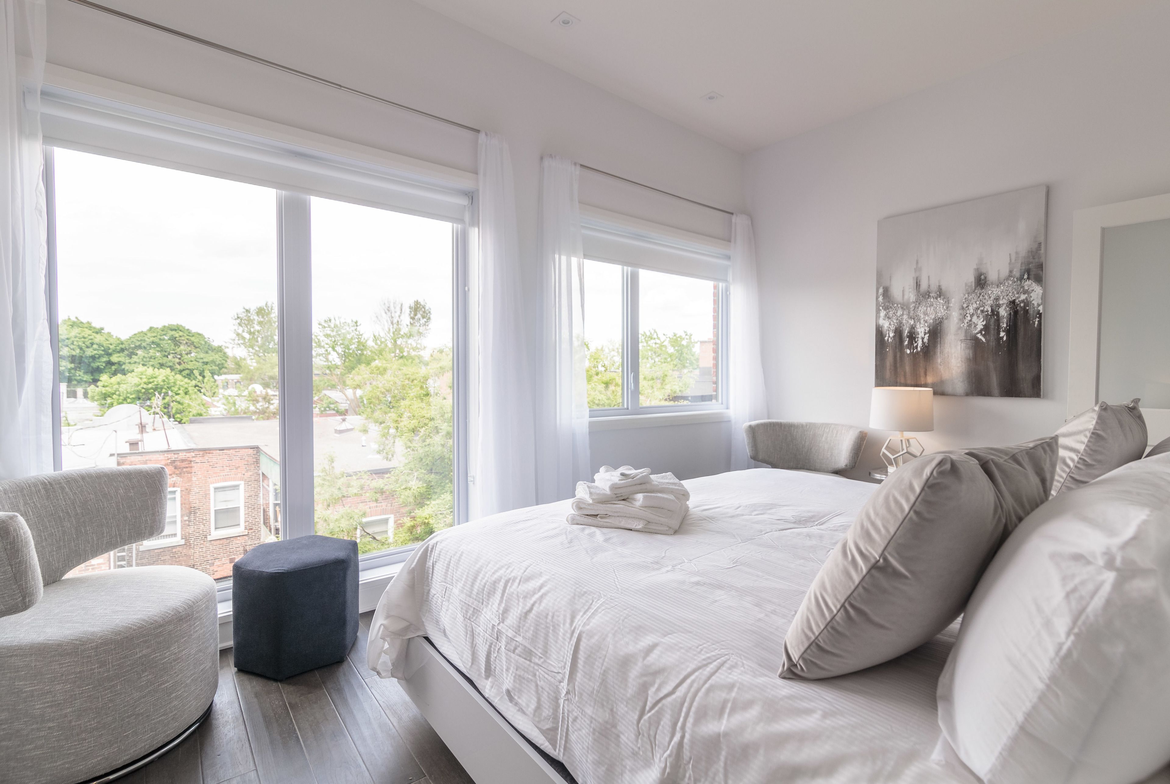Una camera da letto con un letto grande, una poltrona e vista sulla città attraverso ampie finestre.