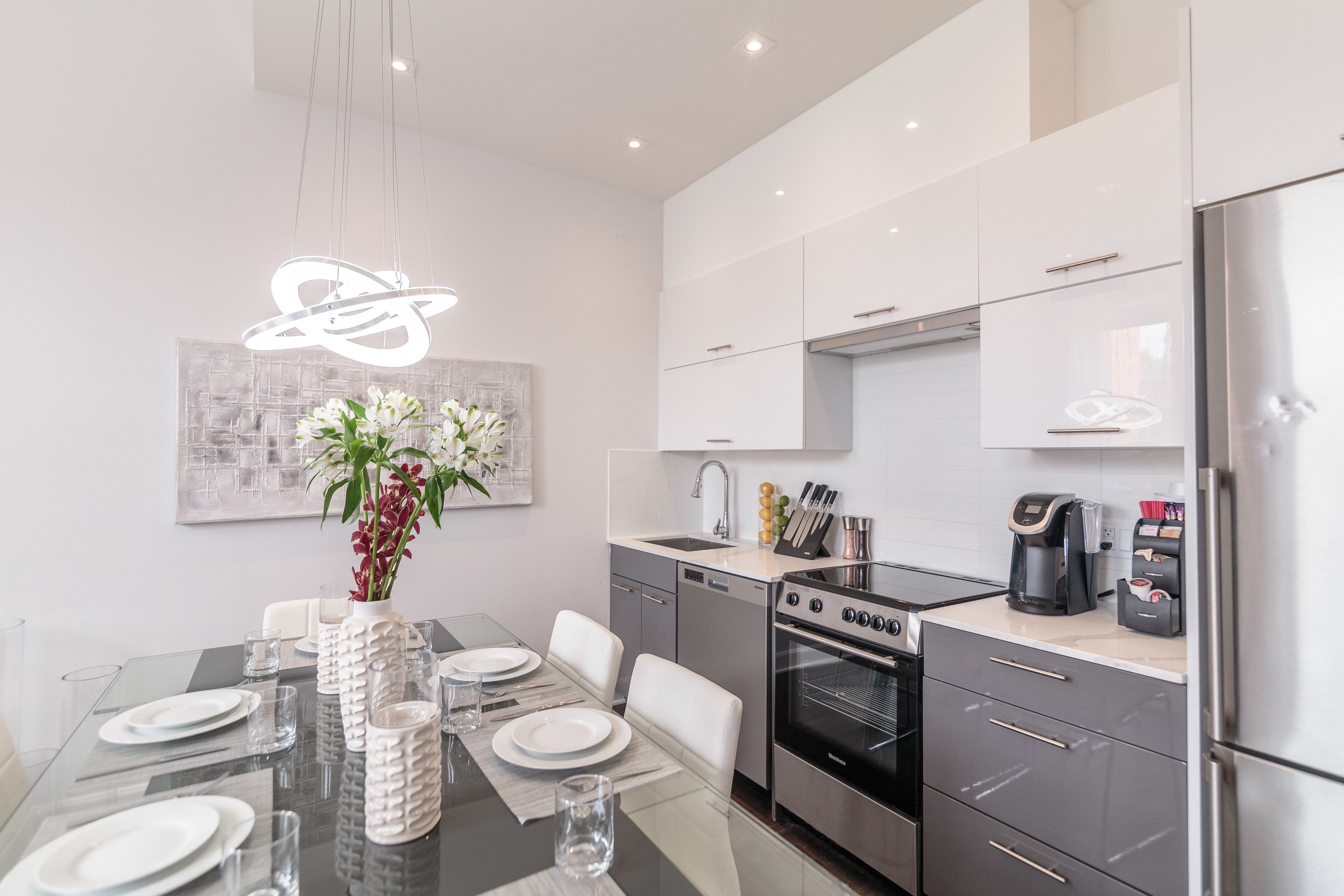 A modern kitchen with a dining area, stainless steel appliances, and a decorative light fixture.