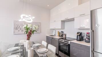 A modern kitchen with a dining area, stainless steel appliances, and a decorative light fixture.
