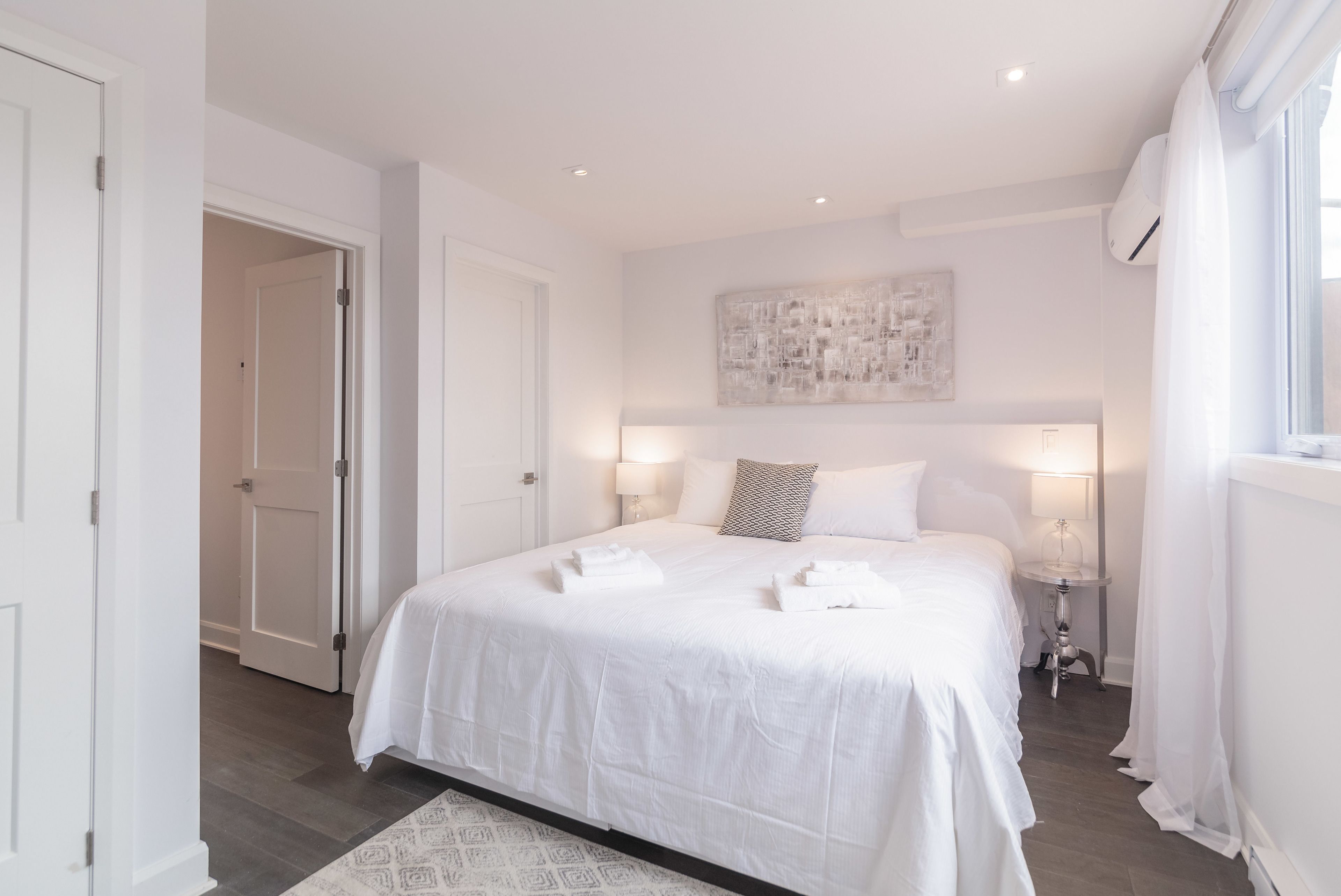 Une chambre d’hôtel avec un grand lit, des lampes de chevet, une œuvre d’art murale et une fenêtre avec des rideaux.