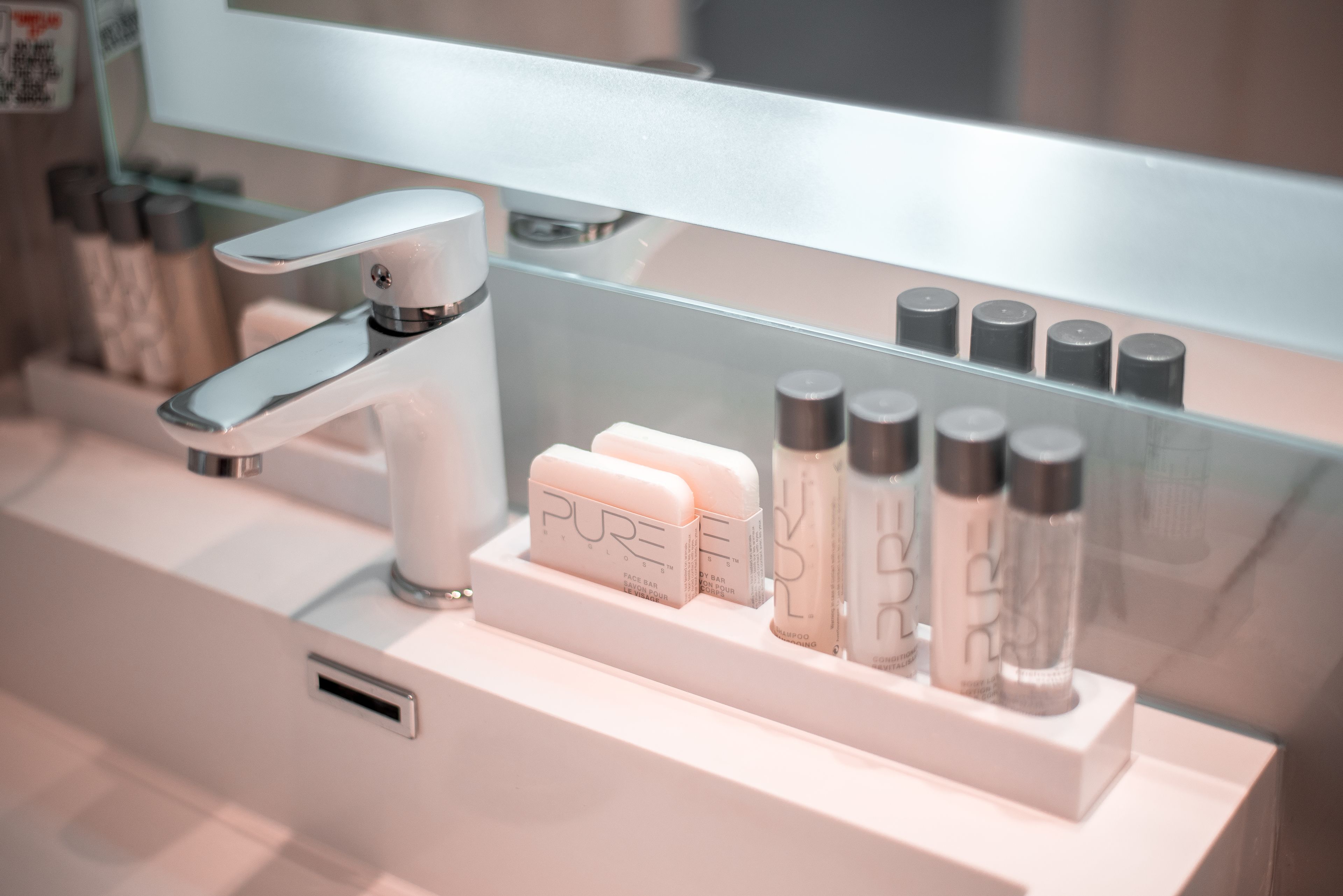 A bathroom with a modern faucet, a mirror, and a shelf with various toiletries.