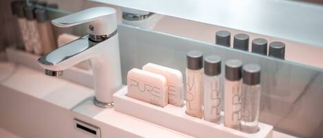 A bathroom with a modern faucet, a mirror, and a shelf with various toiletries.