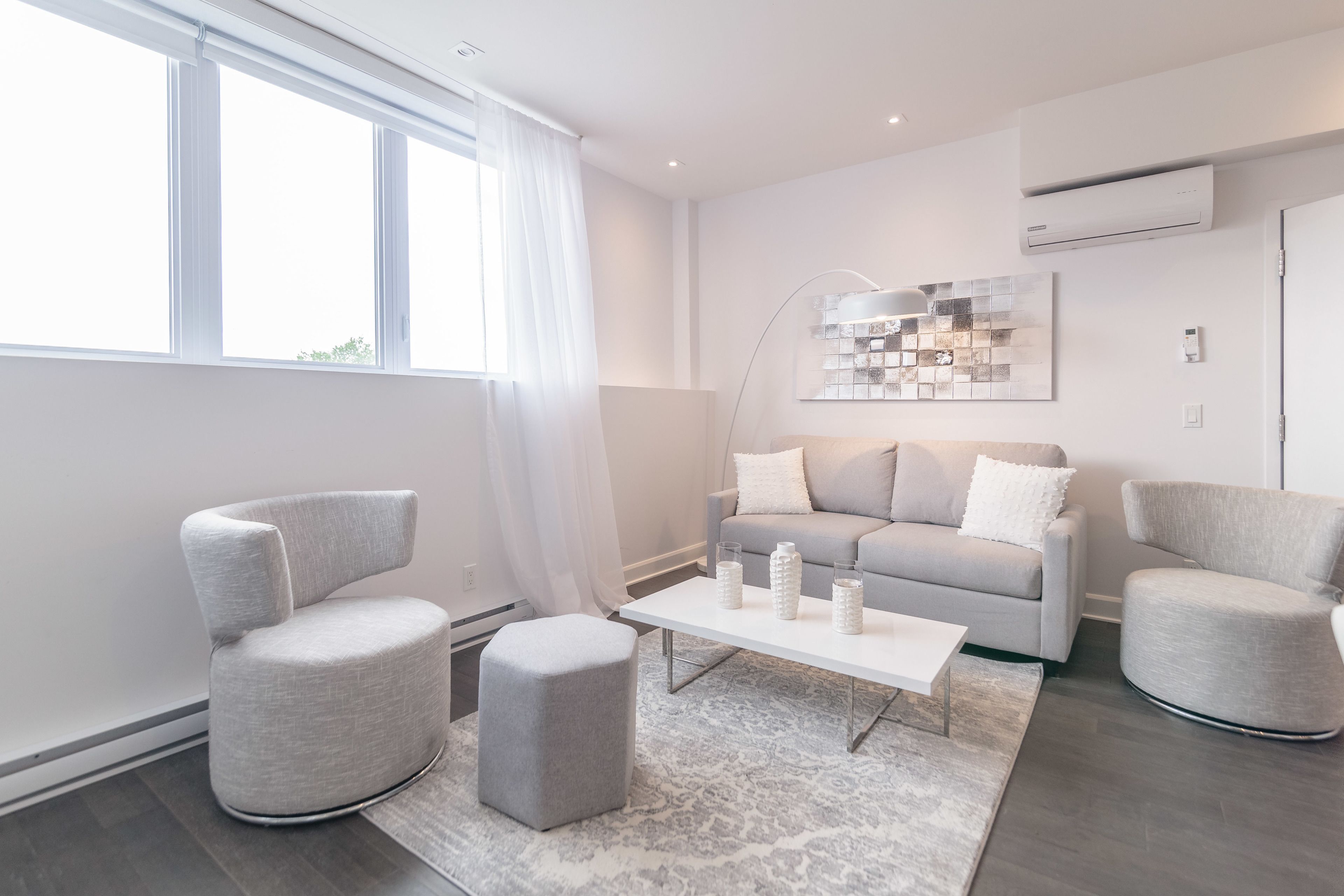 Uma sala de estar moderna com um sofá cinzento, duas poltronas, uma mesa de centro e um tapete estampado.