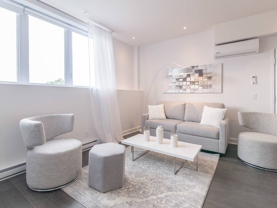 Uma sala de estar moderna com um sofá cinzento, duas poltronas, uma mesa de centro e um tapete estampado.