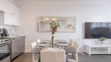 Una cocina moderna con zona de comedor, muebles blancos, electrodomésticos de acero inoxidable y un televisor de pantalla plana.