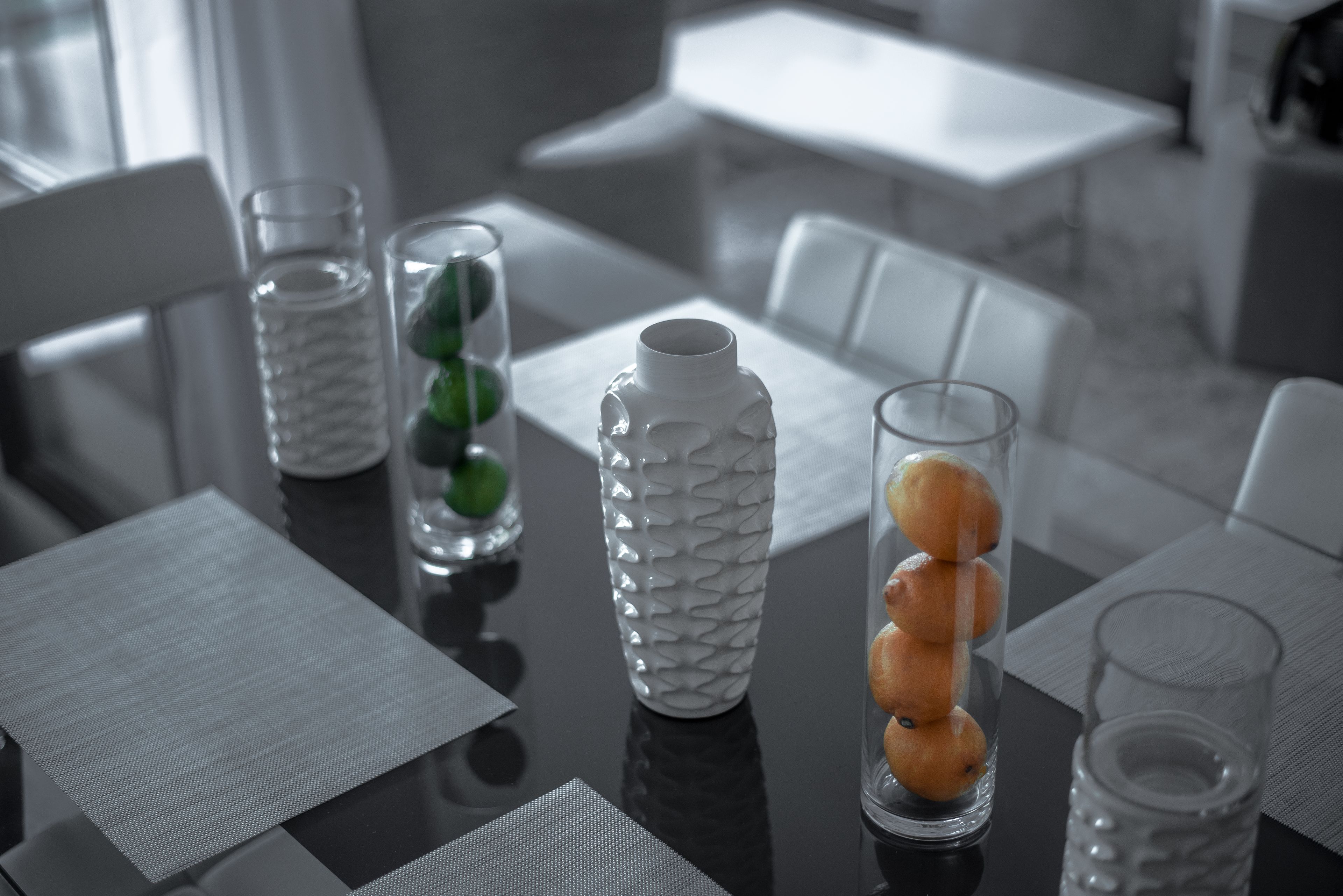 Une table à manger agrémentée d’un vase blanc à texture, de vases en verre transparent contenant des objets verts et d’un vase en verre transparent contenant des objets orange.