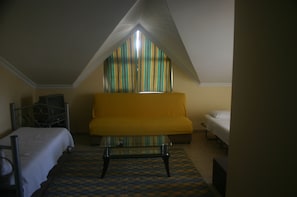 Een kamer met een bed, een gele bank, een glazen salontafel en een raam met gestreepte gordijnen.