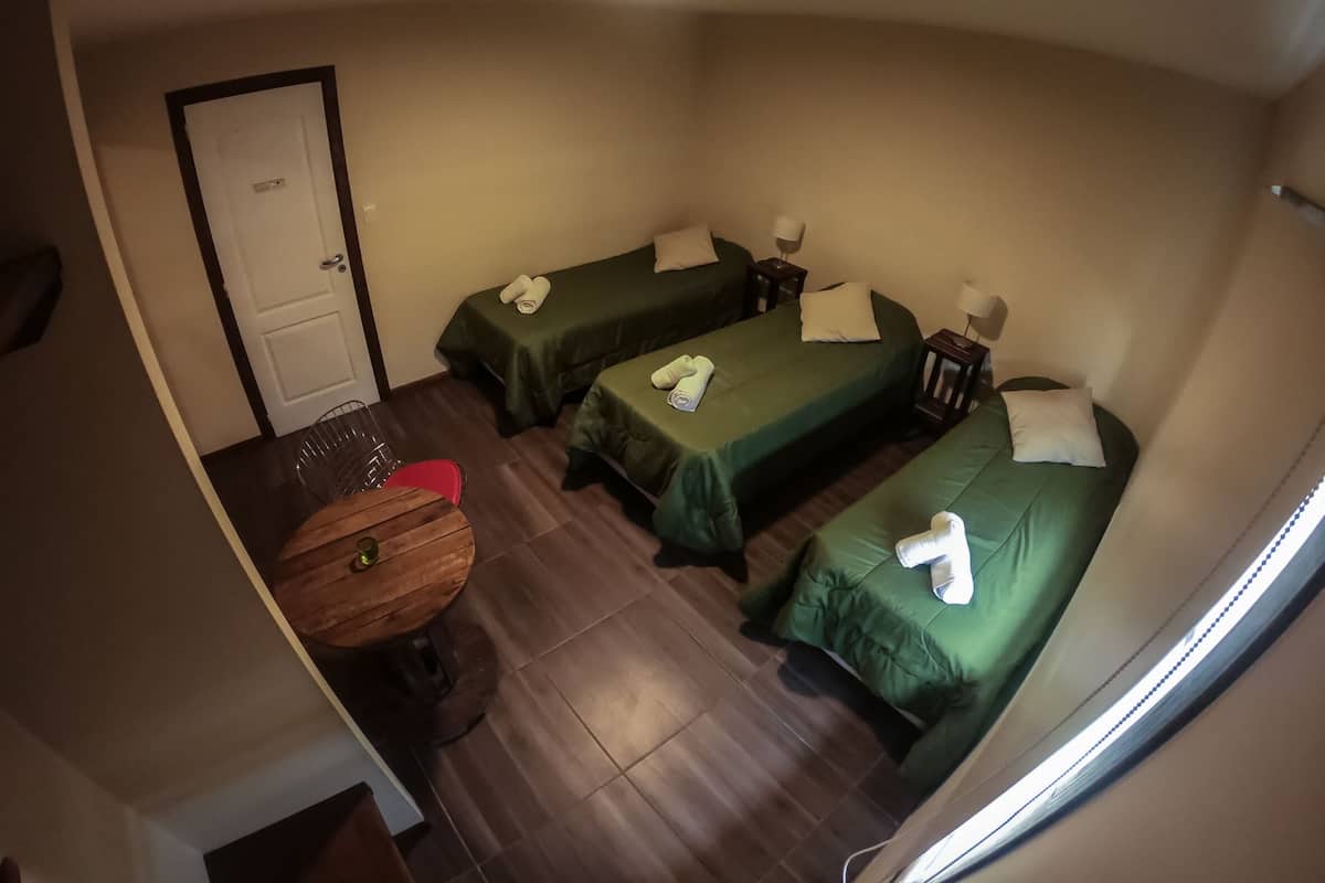 A hotel room with three single beds, a wooden table, and a door.