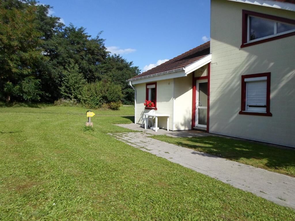 A house with a red door and white walls, a small porch, and a grassy yard.