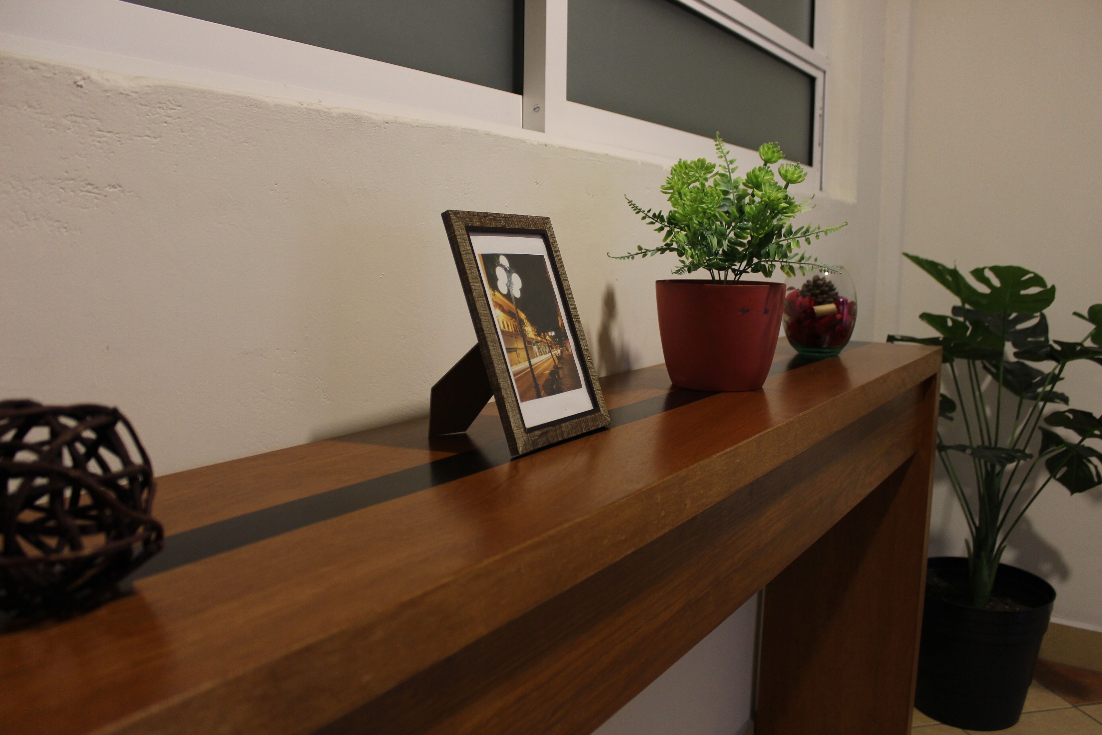 Un mostrador de recepción de madera con un marco de fotos, una planta en maceta y un objeto decorativo.