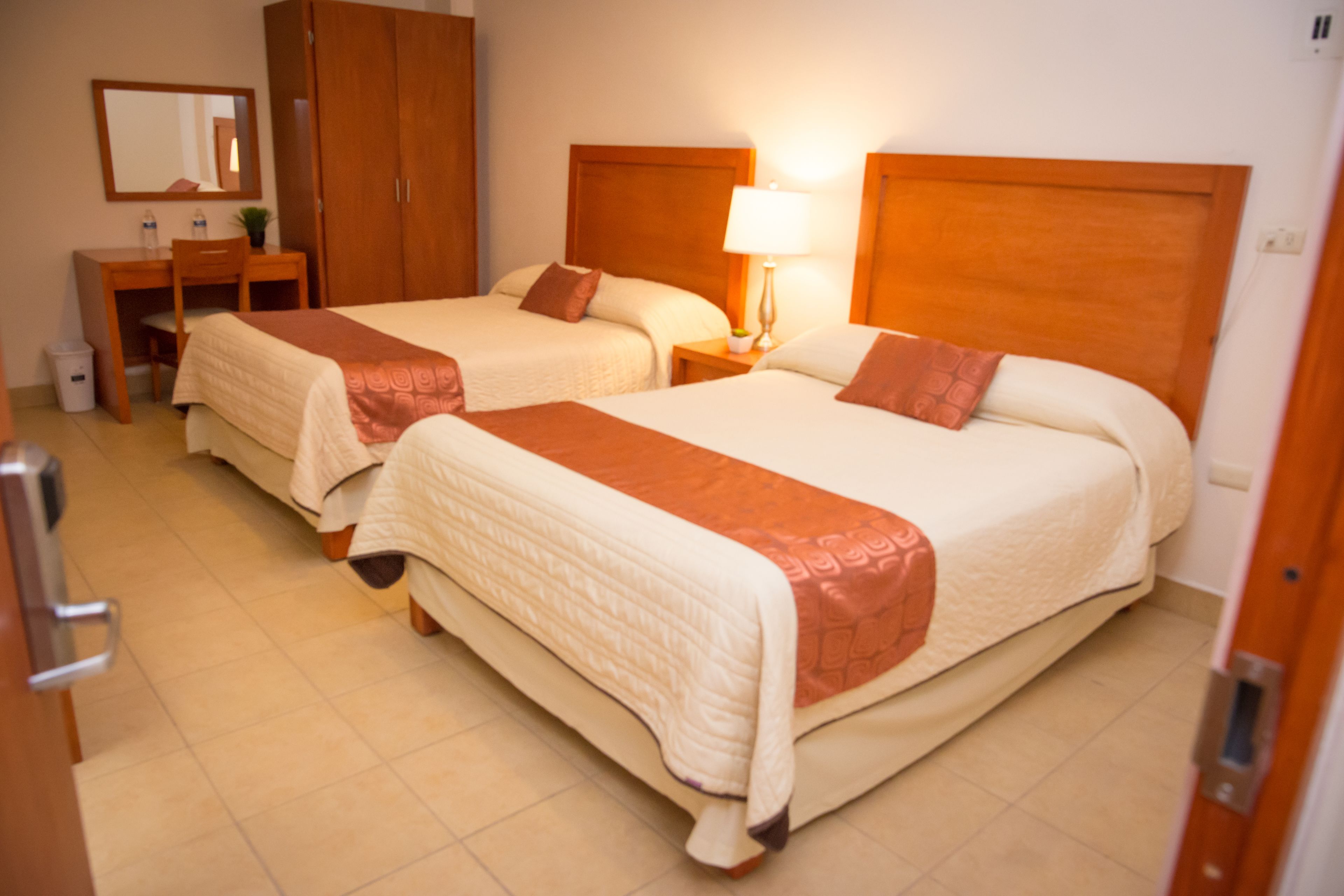 A hotel room with two beds, a desk, and a mirror.