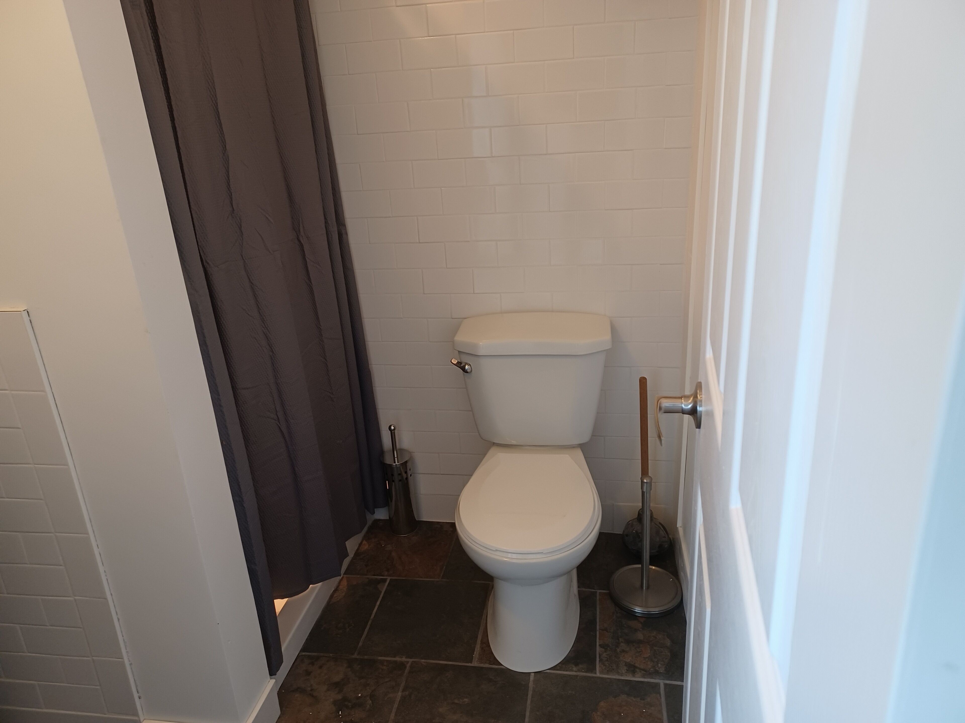 A small, clean bathroom with a white toilet, dark brown shower curtain, and tiled walls.